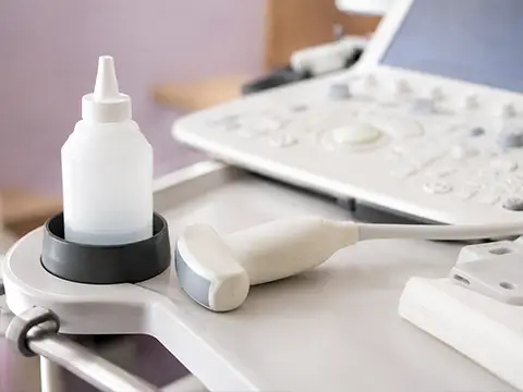 Transdutor e frasco de gel prontos ao lado do aparelho de ultrassonografia